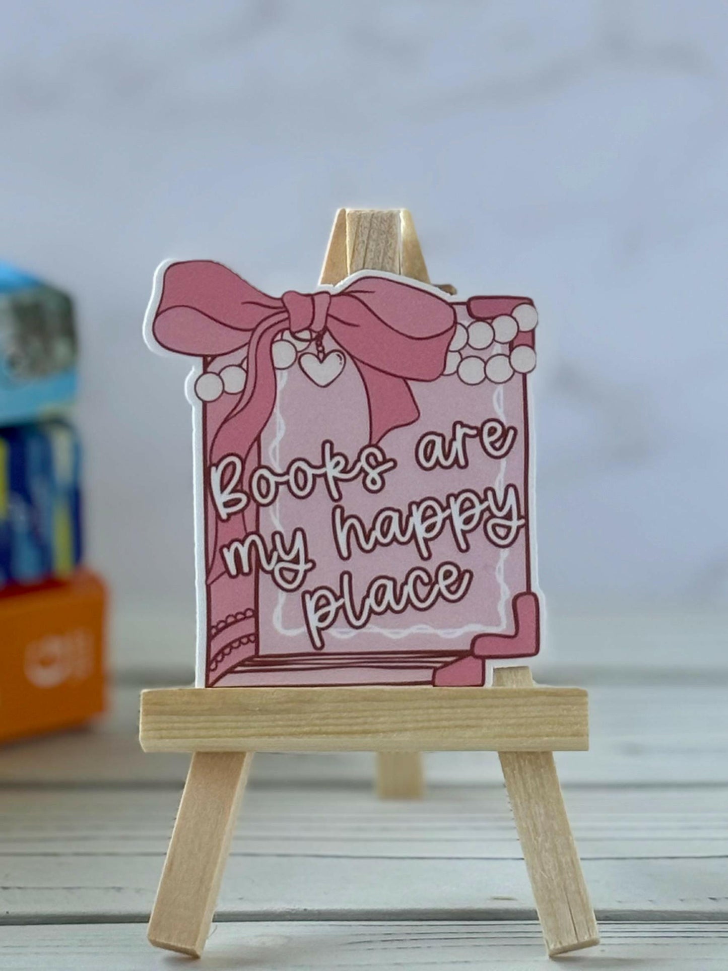 Coquette-style pink book sticker with a bow and pearls. White cursive text reads “Books are my happy place.”