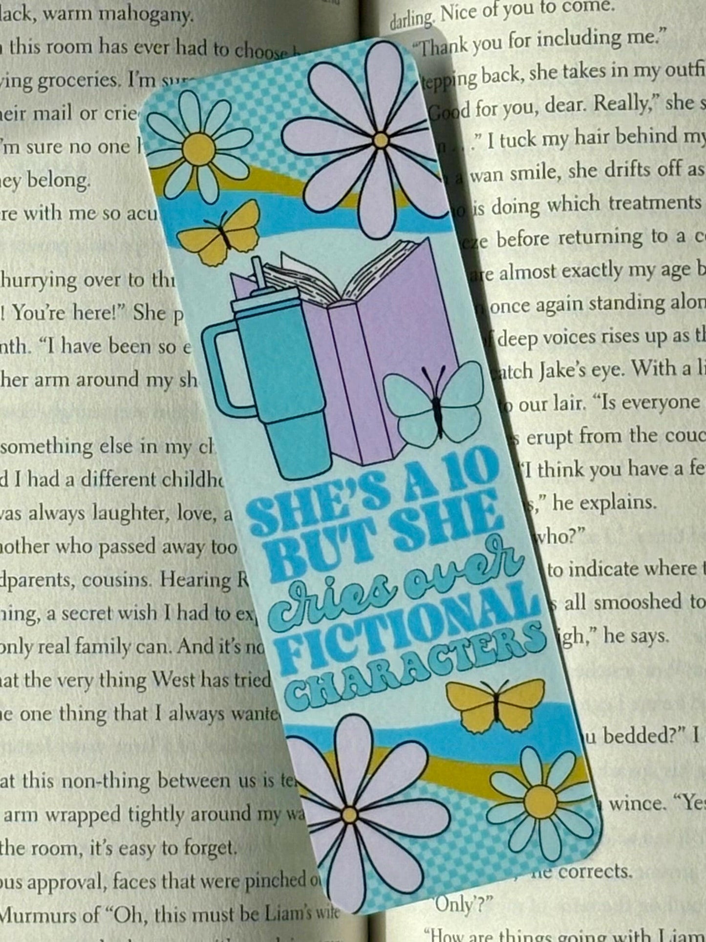 Colorful bookmark with floral designs and text reading “She’s A 10 But She cries over Fictional Characters” on a book page background