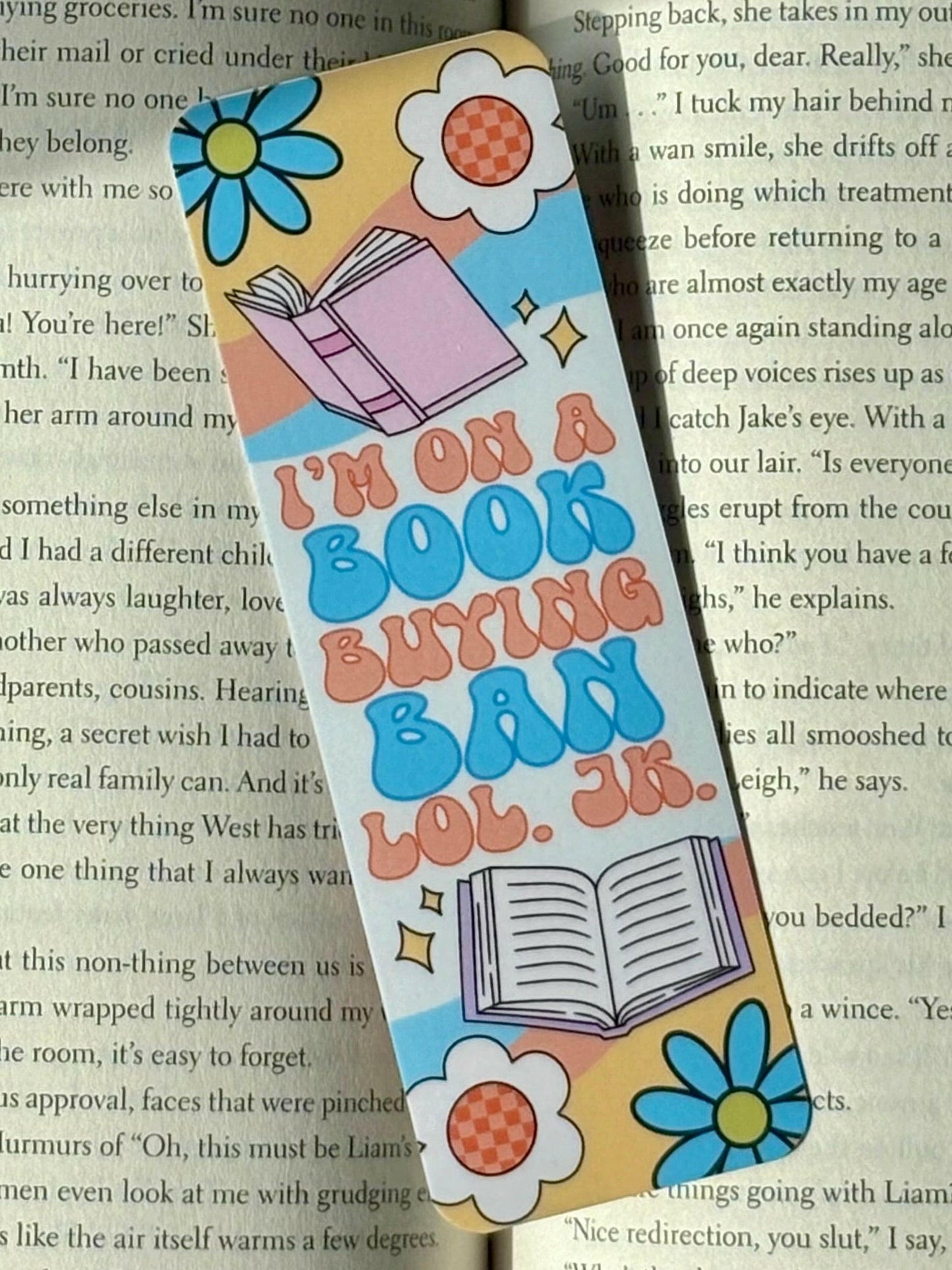 Colorful bookmark with text saying “I’m On A Book Buying Ban LOL. JK.” and floral designs on a book page