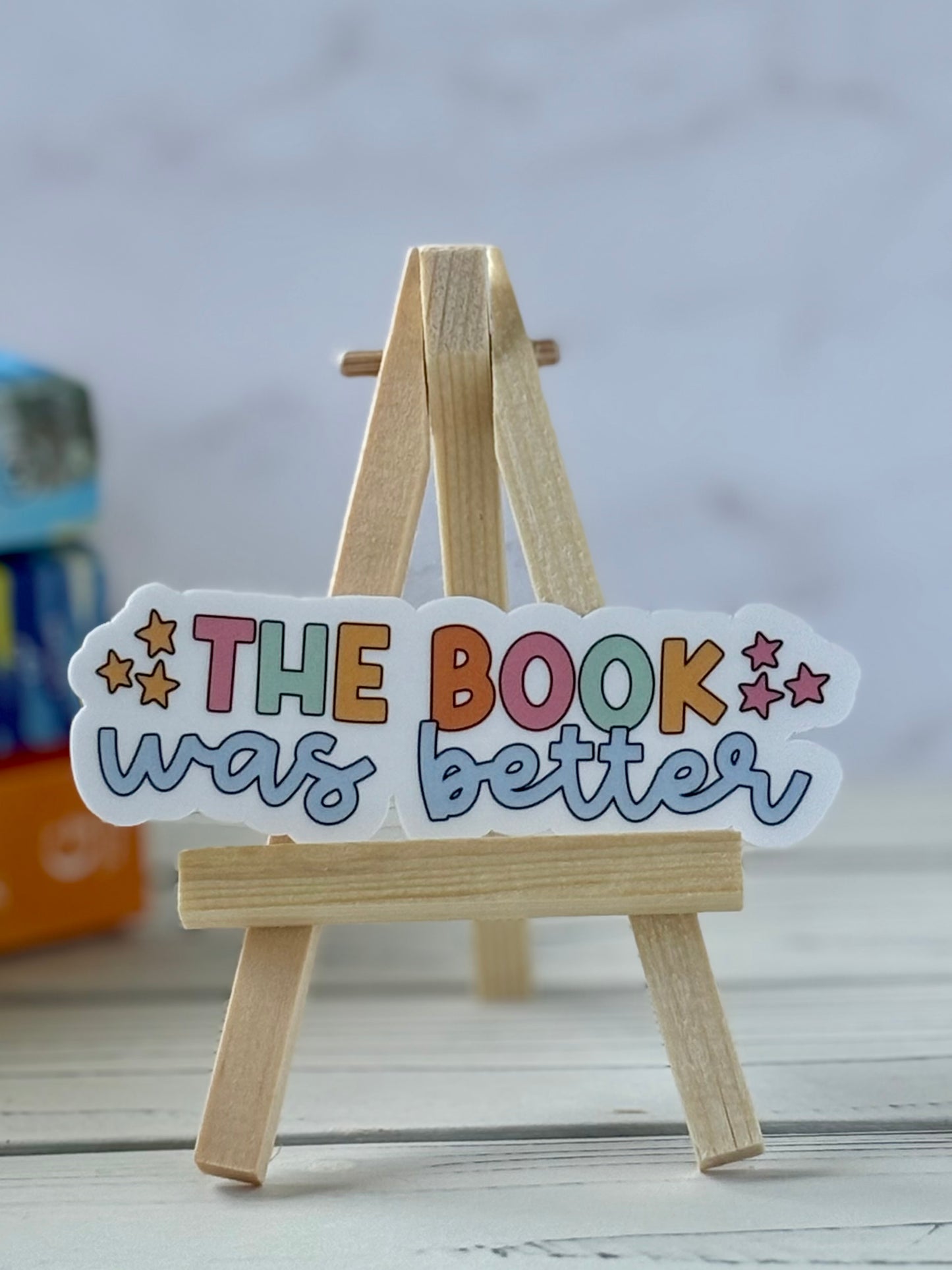 Colorful sign on a wooden stand with 'The Book was better' text against a blurred background