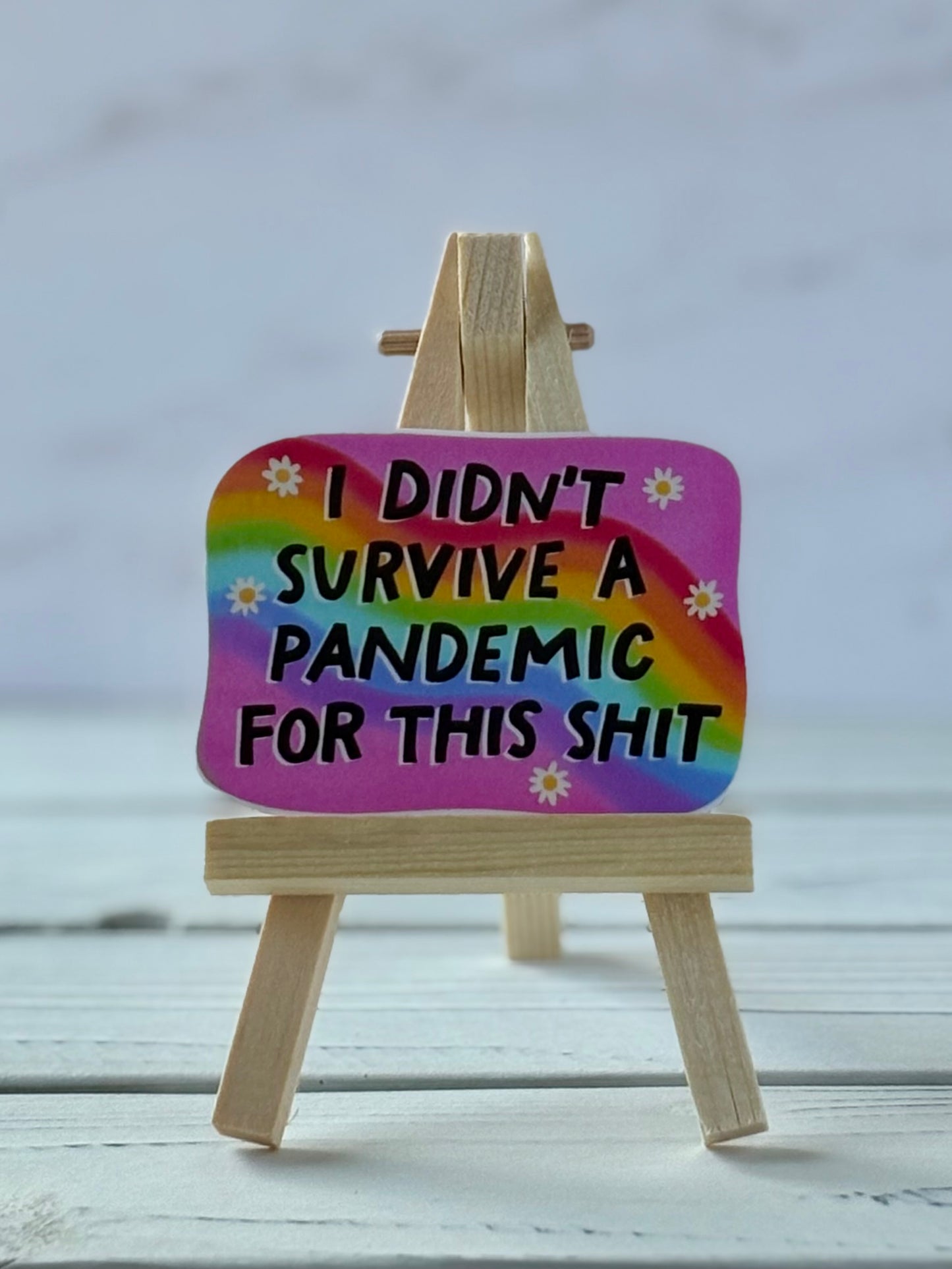 Pink sticker with rainbow, daisies, and black text reading “I Didn’t Survive a Pandemic for This Shit”