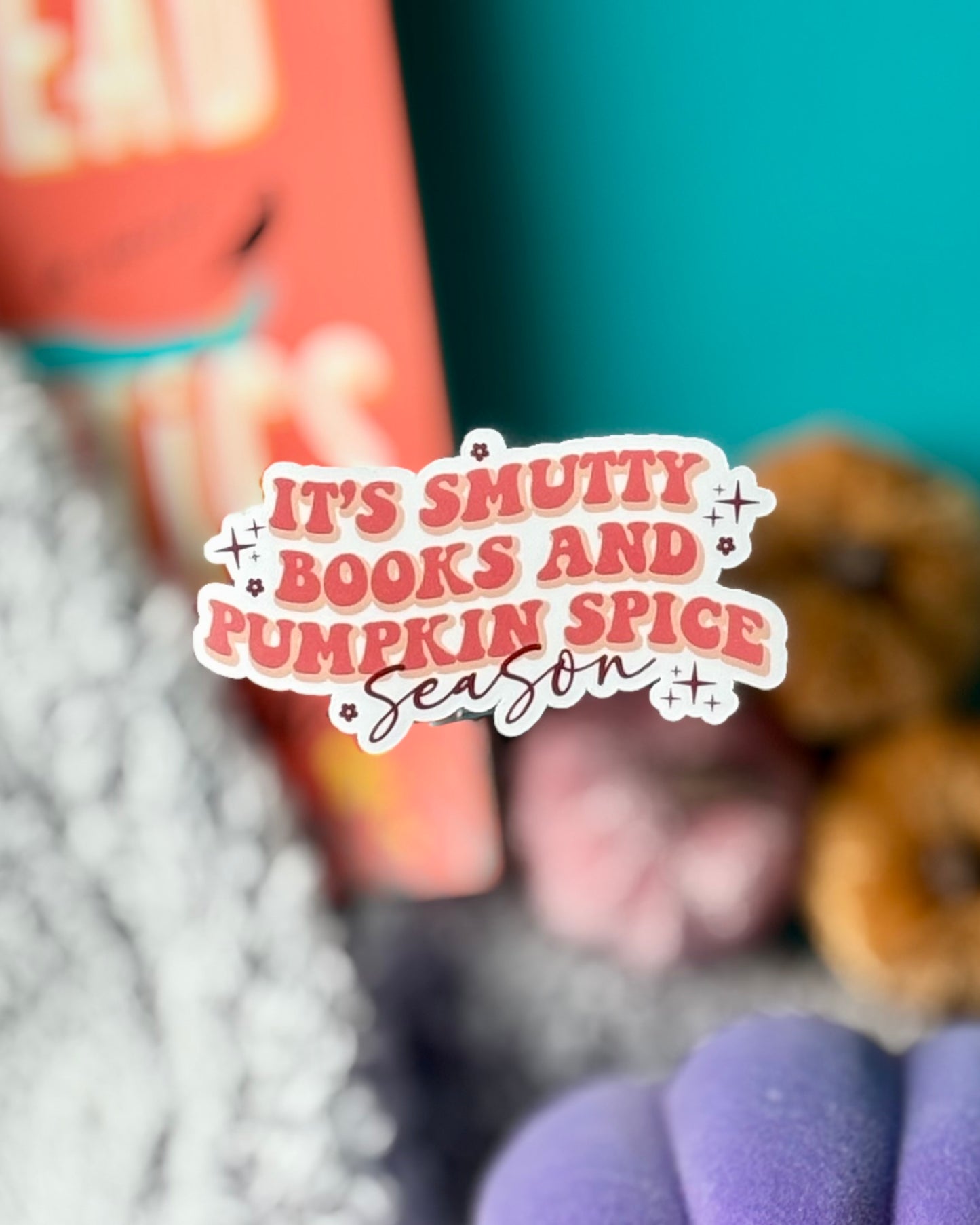 Sticker that says “It’s Smutty Books And Pumpkin Spice Season” in retro orange text on white vinyl