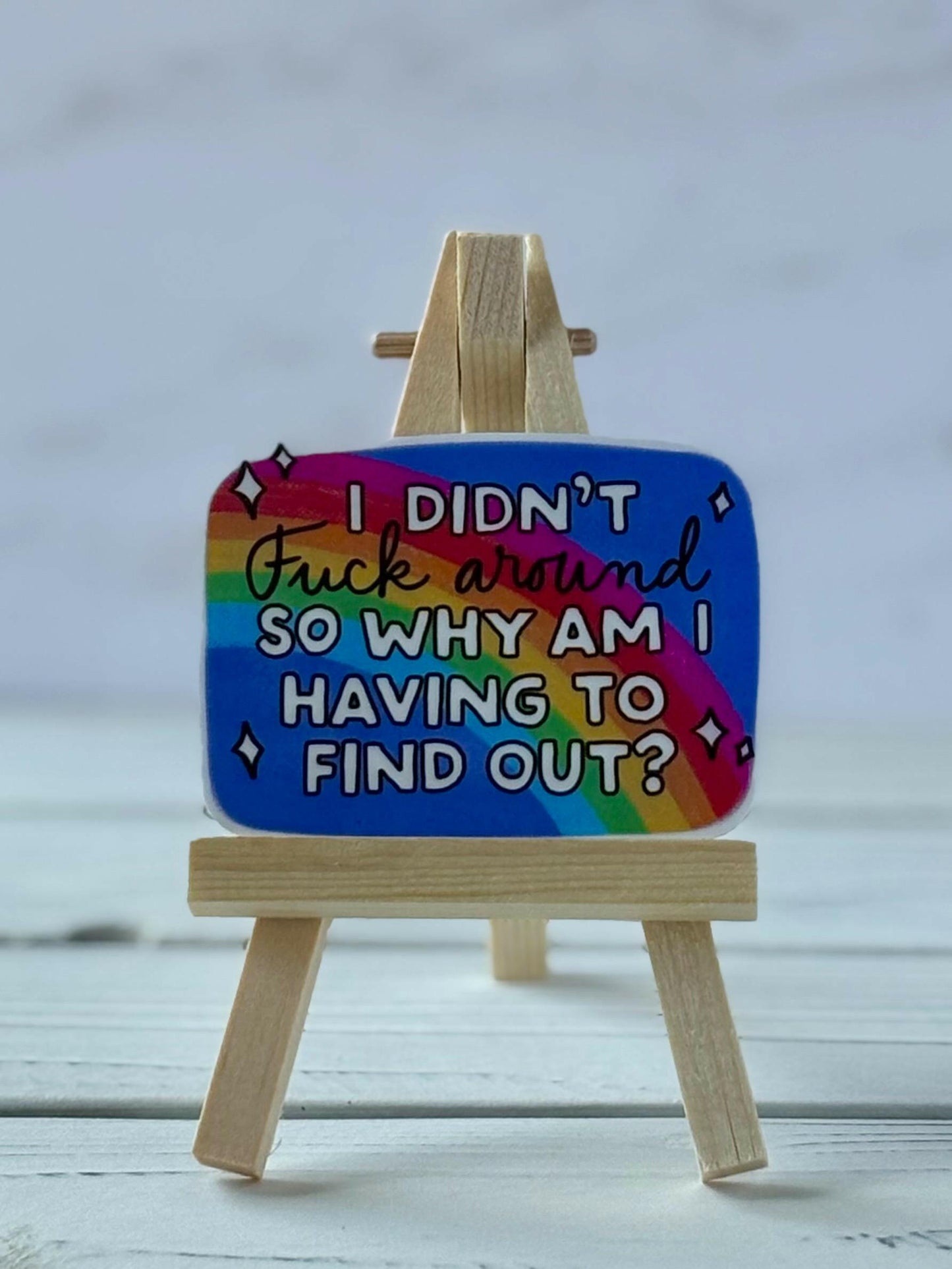 Snarky rainbow sticker with blocky white text that reads “I Didn’t Fuck Around So Why Am I Having To Find Out?” on a blue sky background