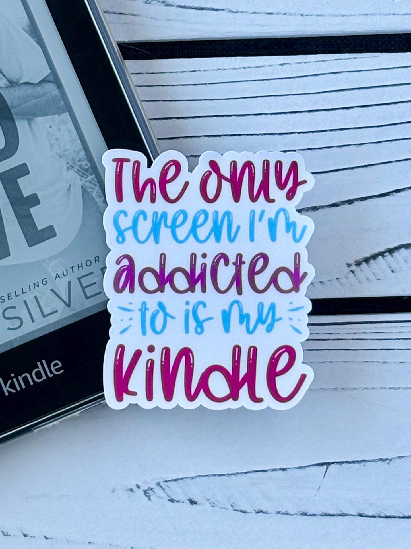 Sticker that says ‘The Only Screen I’m Addicted to Is My Kindle’ in colorful retro text on a white background