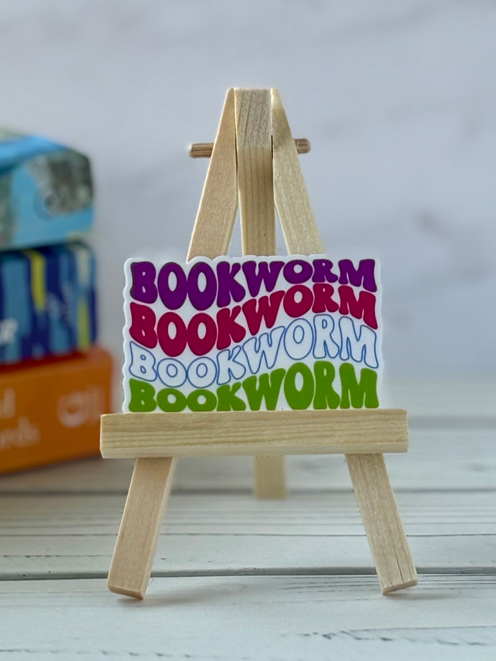 Colorful 'bookworm' retro vinyl sticker on a small wooden easel with a blurred background