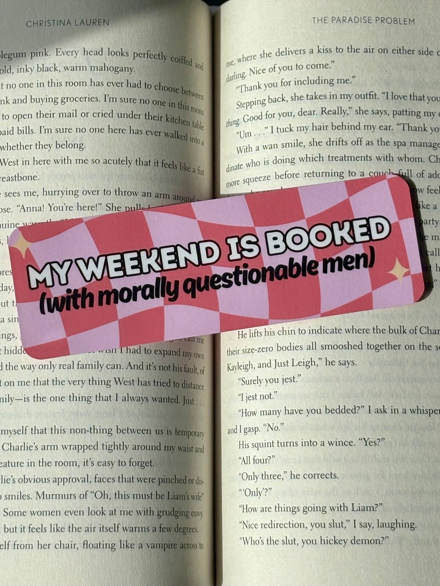Checkered bookmark with text 'My weekend is booked (with morally questionable men)' on a book page.