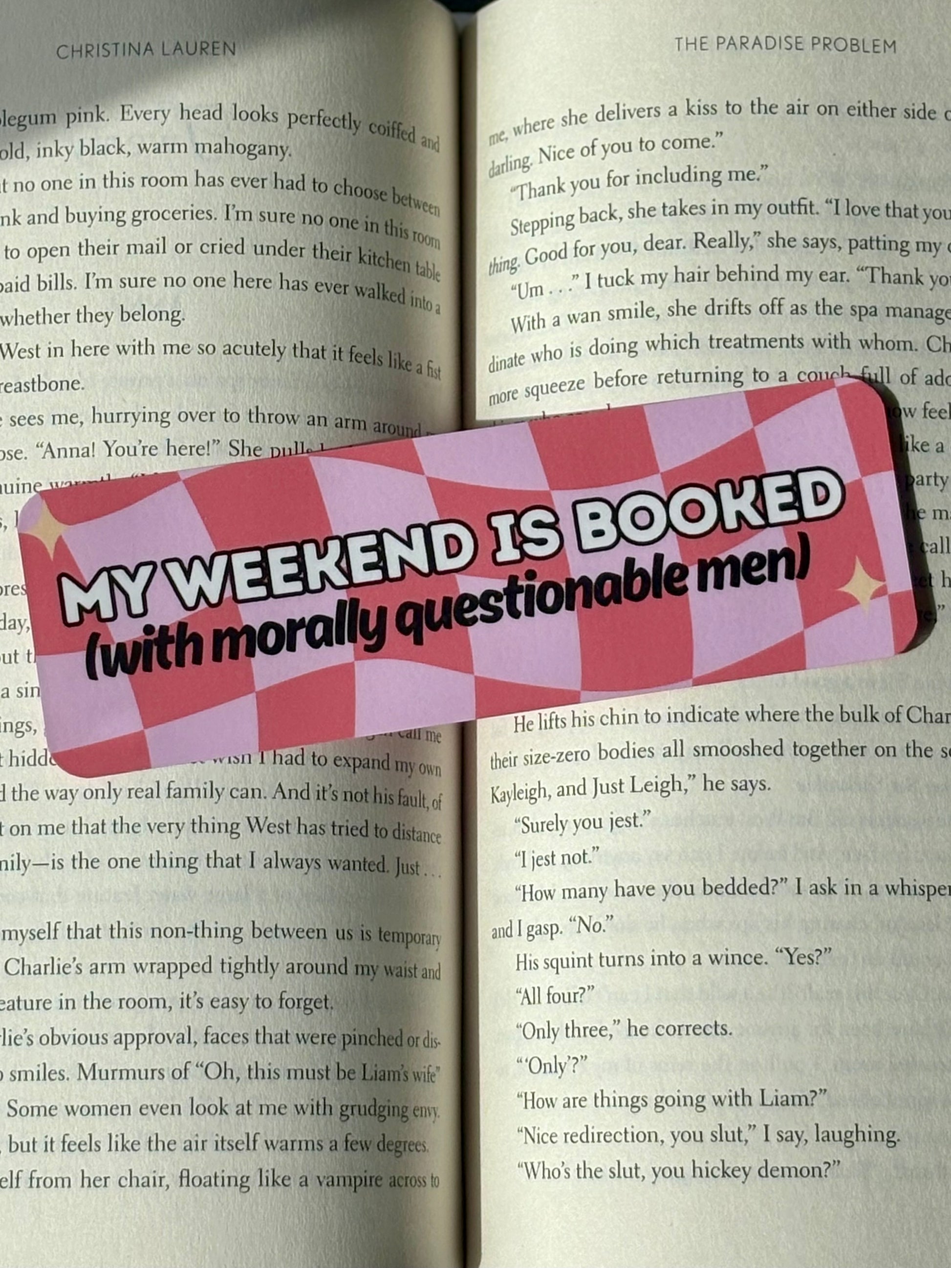 Checkered bookmark with text 'My weekend is booked (with morally questionable men)' on a book page.