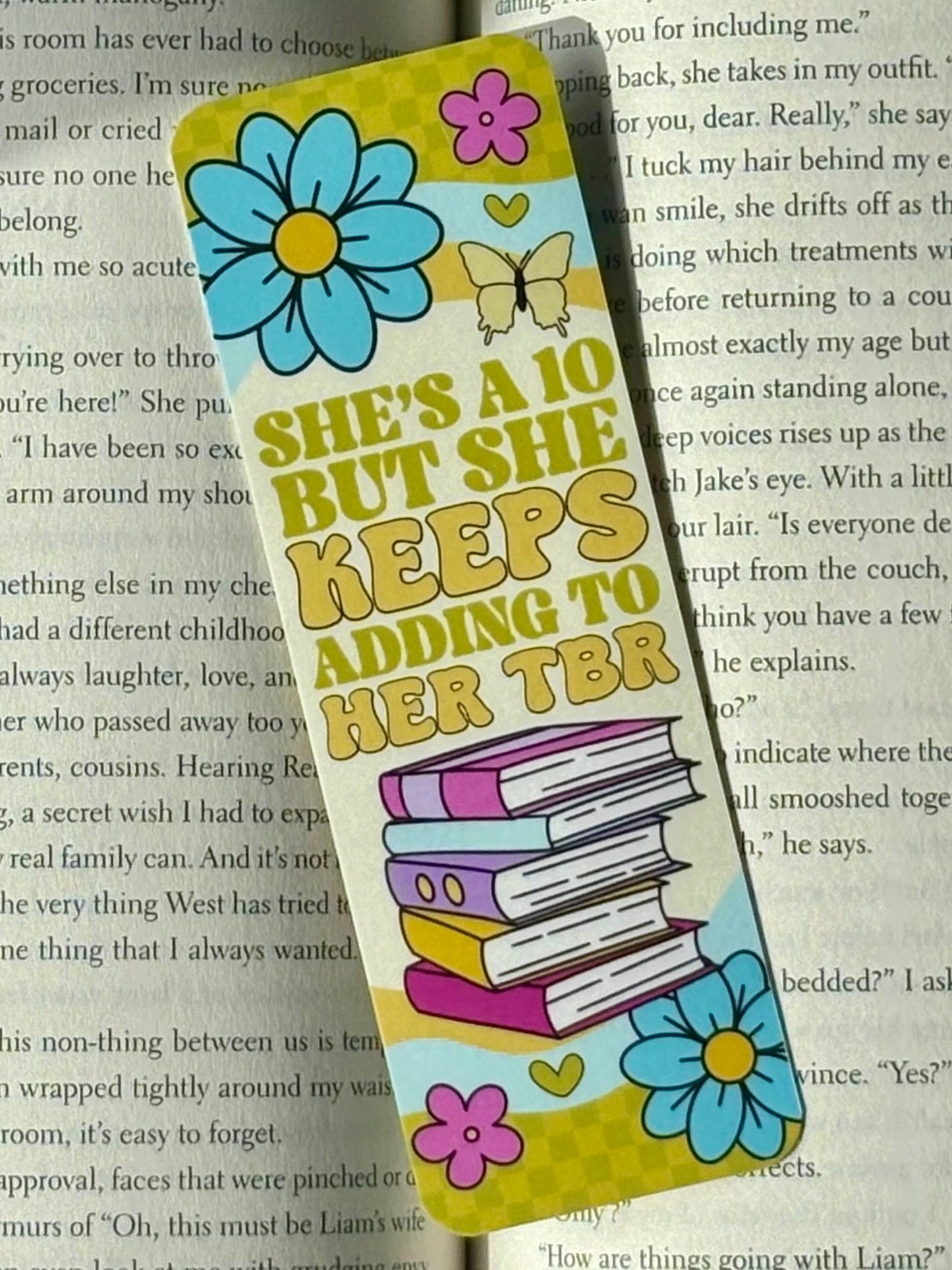 Colorful bookmark with floral designs and text reading “She’s A 10 But She Keeps Adding To Her TBR” on a book page background