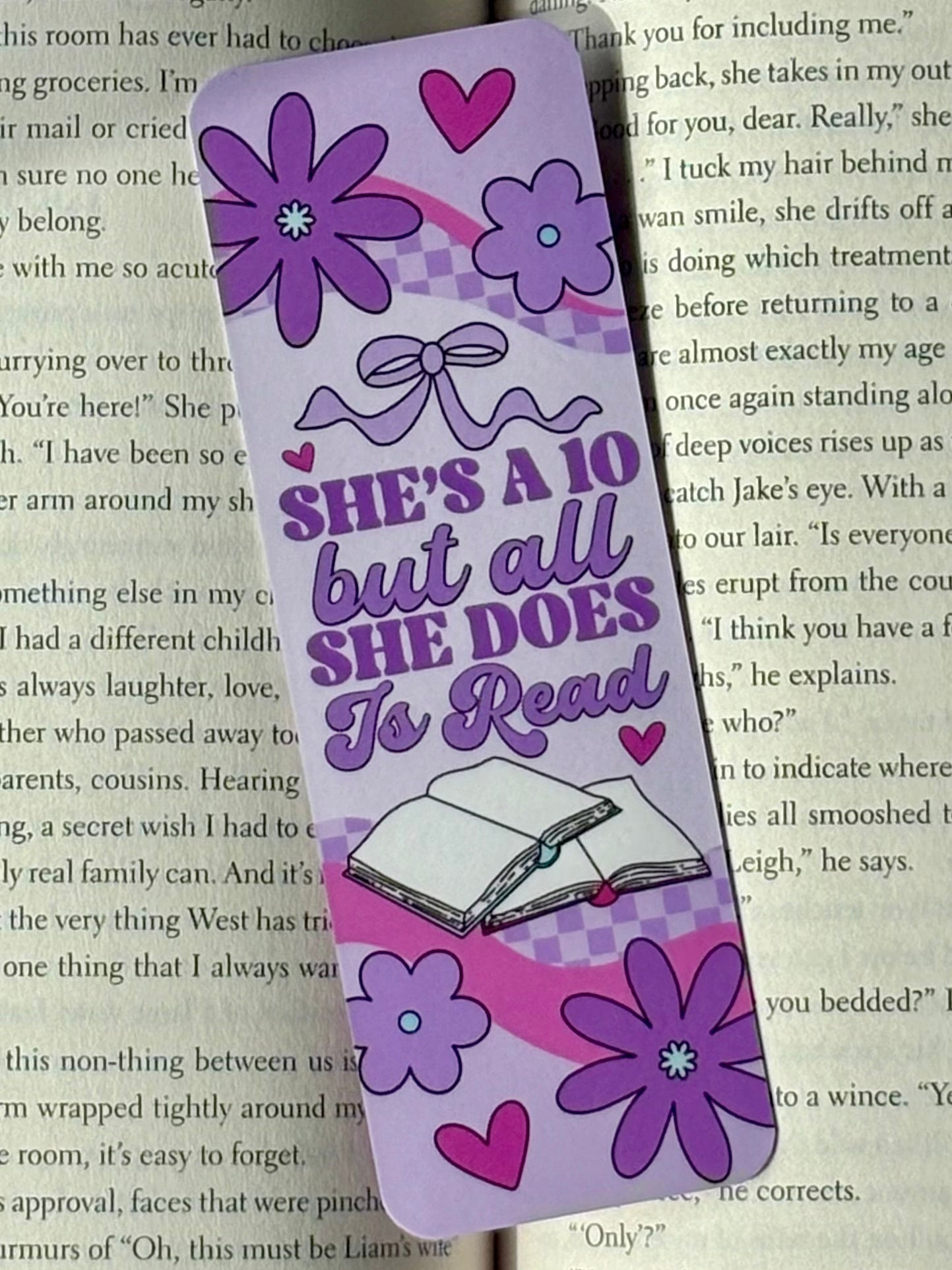 Purple bookmark with floral designs and text reading “She’s A 10 but all She Does Is Read” on a book page background