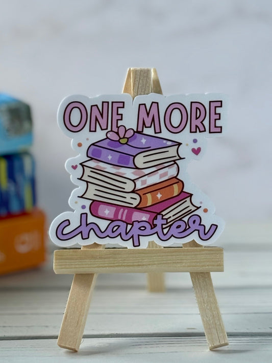 Decorative sticker with 'One More Chapter' text and book illustration on a small wooden stand.