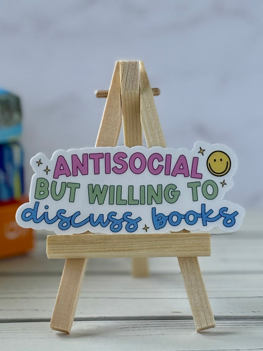 Wooden easel with a colorful sign reading 'Antisocial but willing to discuss books' on a light background.