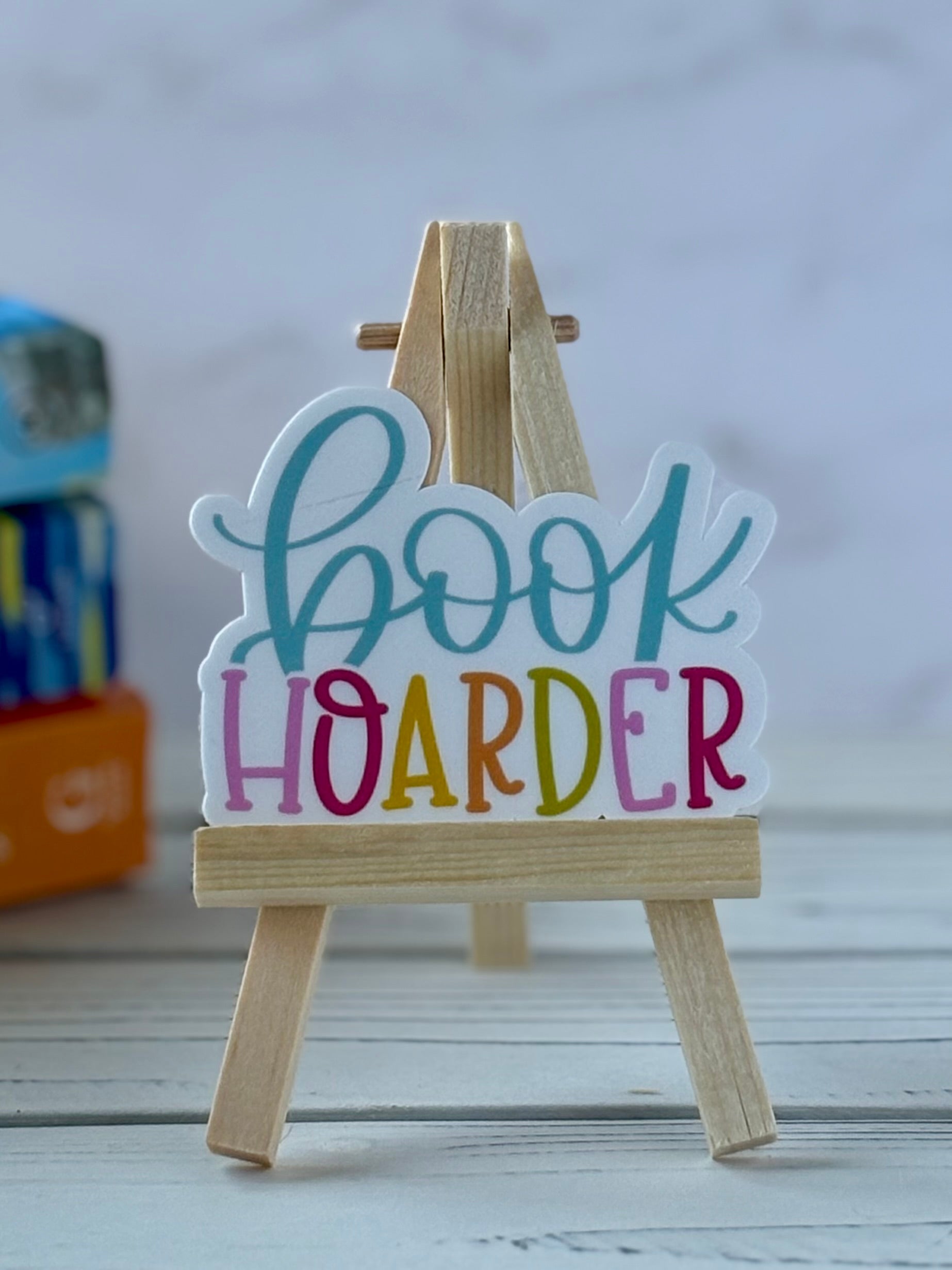 Colorful 'book hoarder' sign on a small wooden easel against a neutral background