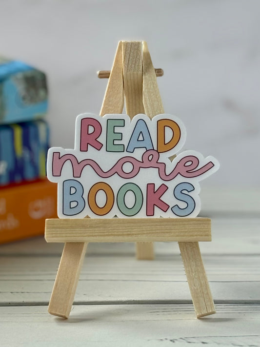 Colorful 'Read more books' sign on a small wooden easel with a blurred bookshelf background.