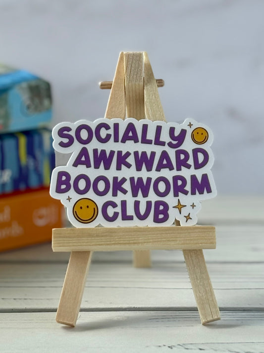 Sticker with 'Socially Awkward Bookworm Club' text on a wooden stand against a neutral background