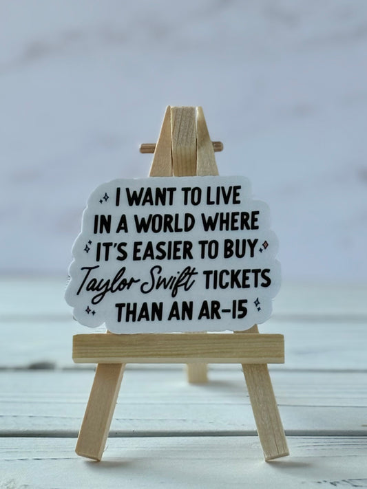 White sticker with black text: “I want to live in a world where it’s easier to buy Taylor Swift tickets than an AR-15”