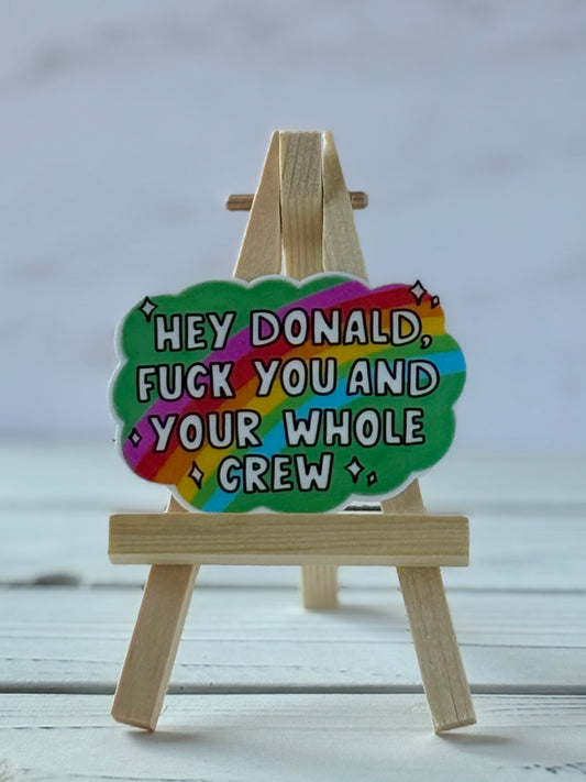 Cloud-shaped sticker with rainbow on green background and white text: “Hey Donald, F*ck You and Your Whole Crew”