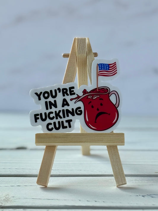 Sticker with black text “You’re in a F*cking Cult” and sad Kool Aid Man holding American flag