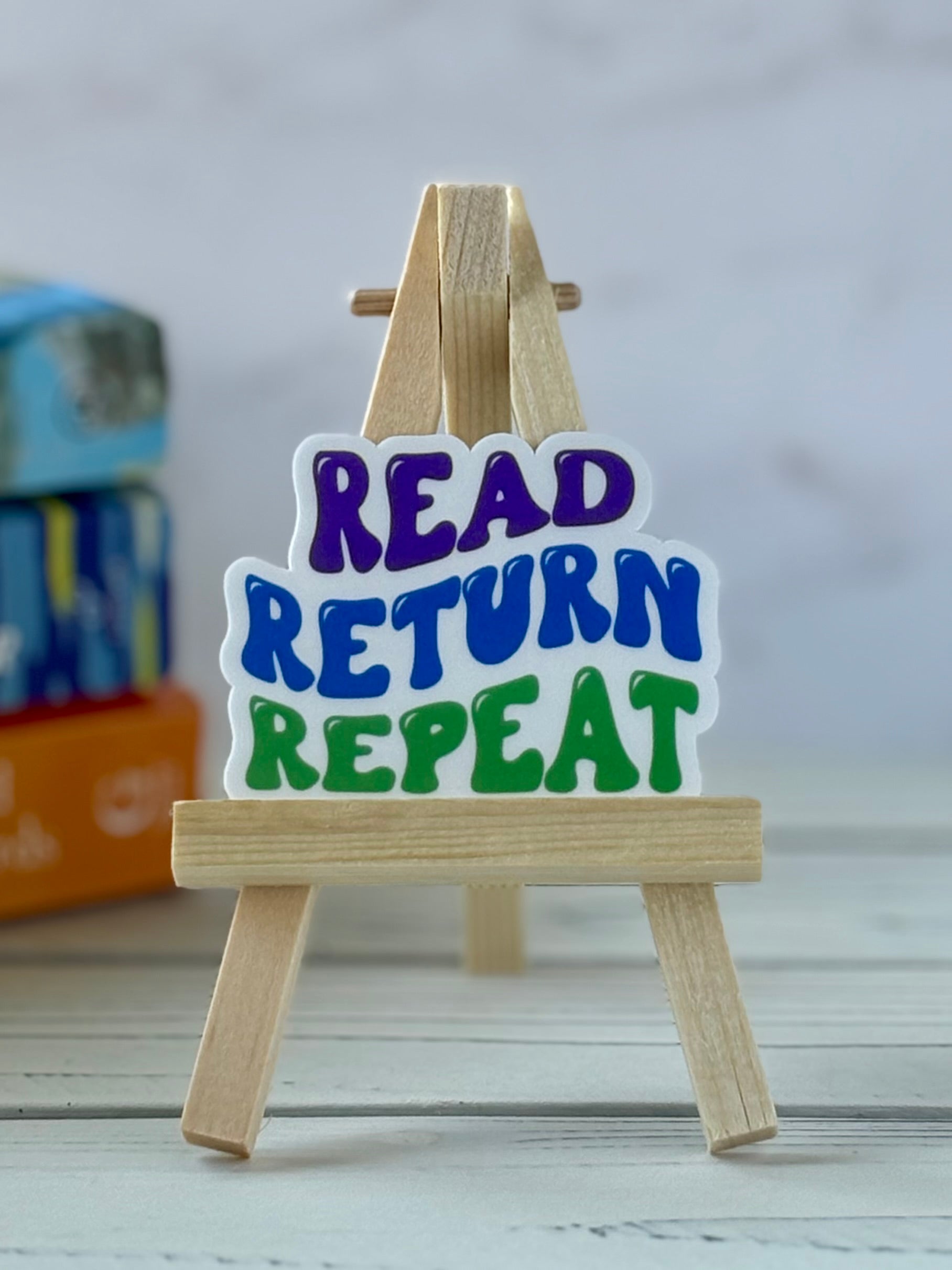 Small wooden easel with 'Read Return Repeat' retro vinyl sticker on a light background